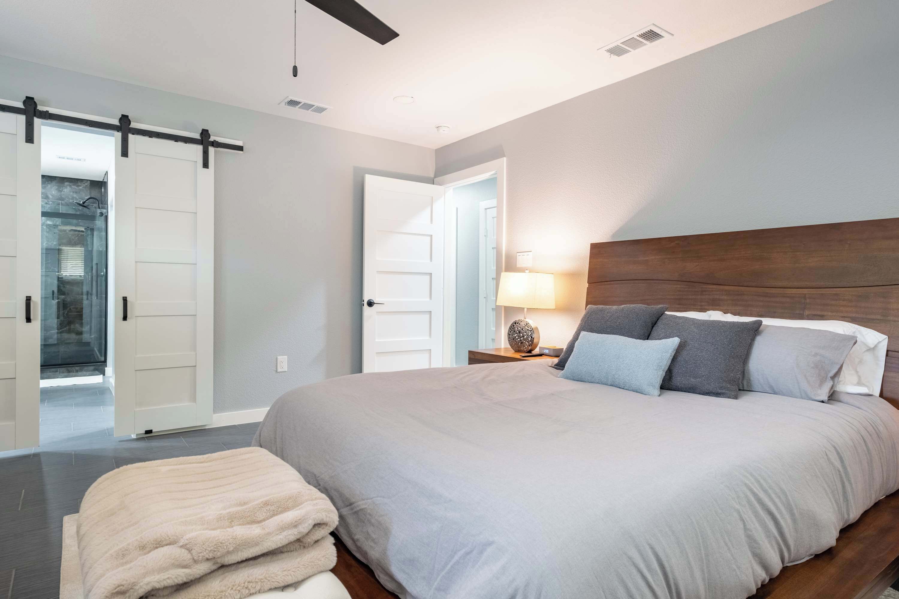 Un dormitorio con una cama grande, una mesita de noche con lámpara y una puerta corredera que da a un baño.