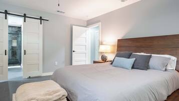 Un dormitorio con una cama grande, una mesita de noche con lámpara y una puerta corredera que da a un baño.