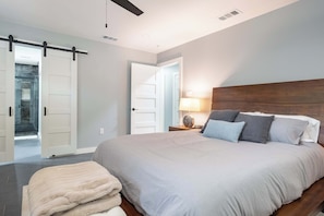 A bedroom with a large bed, a nightstand with a lamp, and a sliding door leading to a bathroom. - Bright Dallas Retreat with Fire Pit & Games (Dallas)