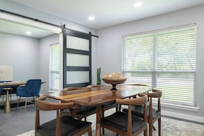 A modern conference room with a wooden table, six chairs, a large window with blinds, and a sliding door. - Bright Dallas Retreat with Fire Pit & Games (Dallas)
