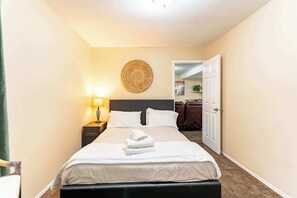Ein Hotelzimmer mit einem Bett, einer Nachttischlampe, einem Wanddekor und einer Tür zu einem anderen Raum.