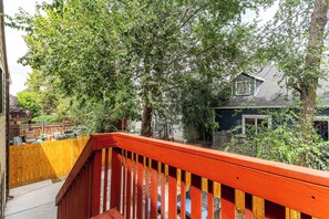 Eine Holzterrasse mit roter Geländer, umgeben von üppigen grünen Bäumen und einem Haus im Hintergrund.