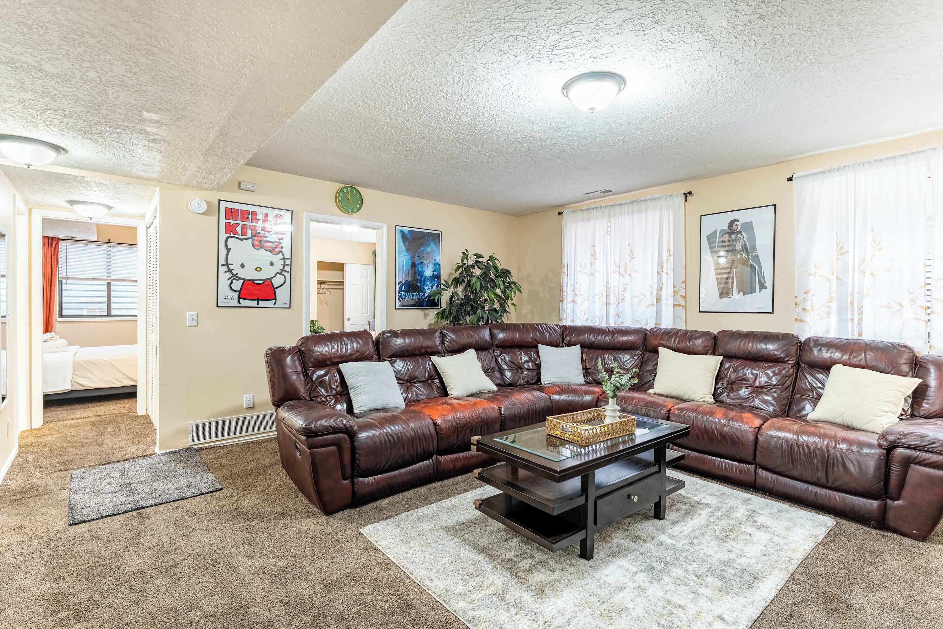 A living room with a brown leather sectional sofa, a coffee table, and a large window with curtains.