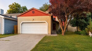 Einbungalow mit Garage, ein Vorgarten mit Rasen und ein Baum mit roten Blättern.