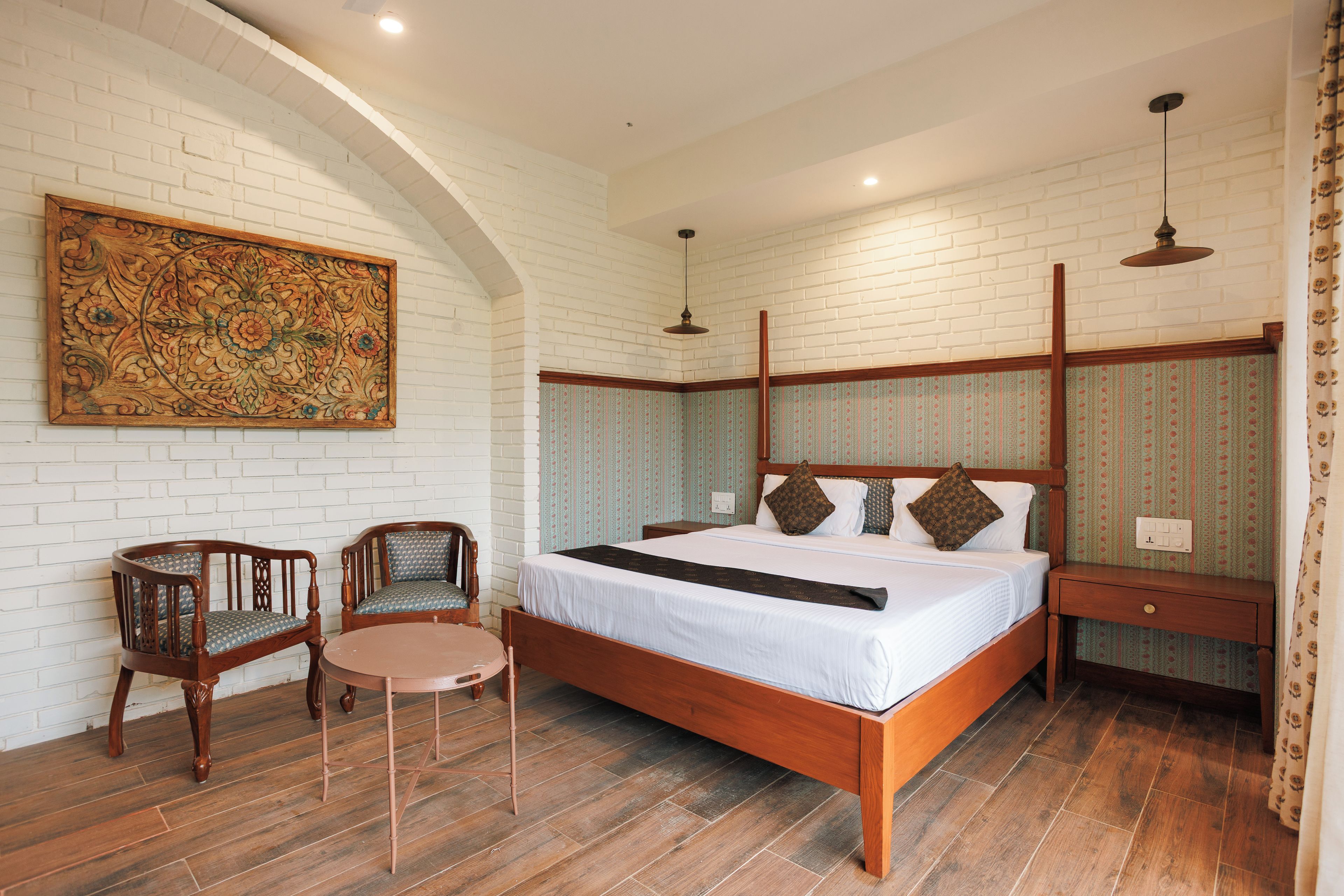 A bedroom with a wooden bed, two chairs, a small table, a decorative wall piece, and patterned wallpaper.