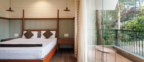 A bedroom with a wooden bed, a nightstand, a small table, and a balcony with a view of greenery.