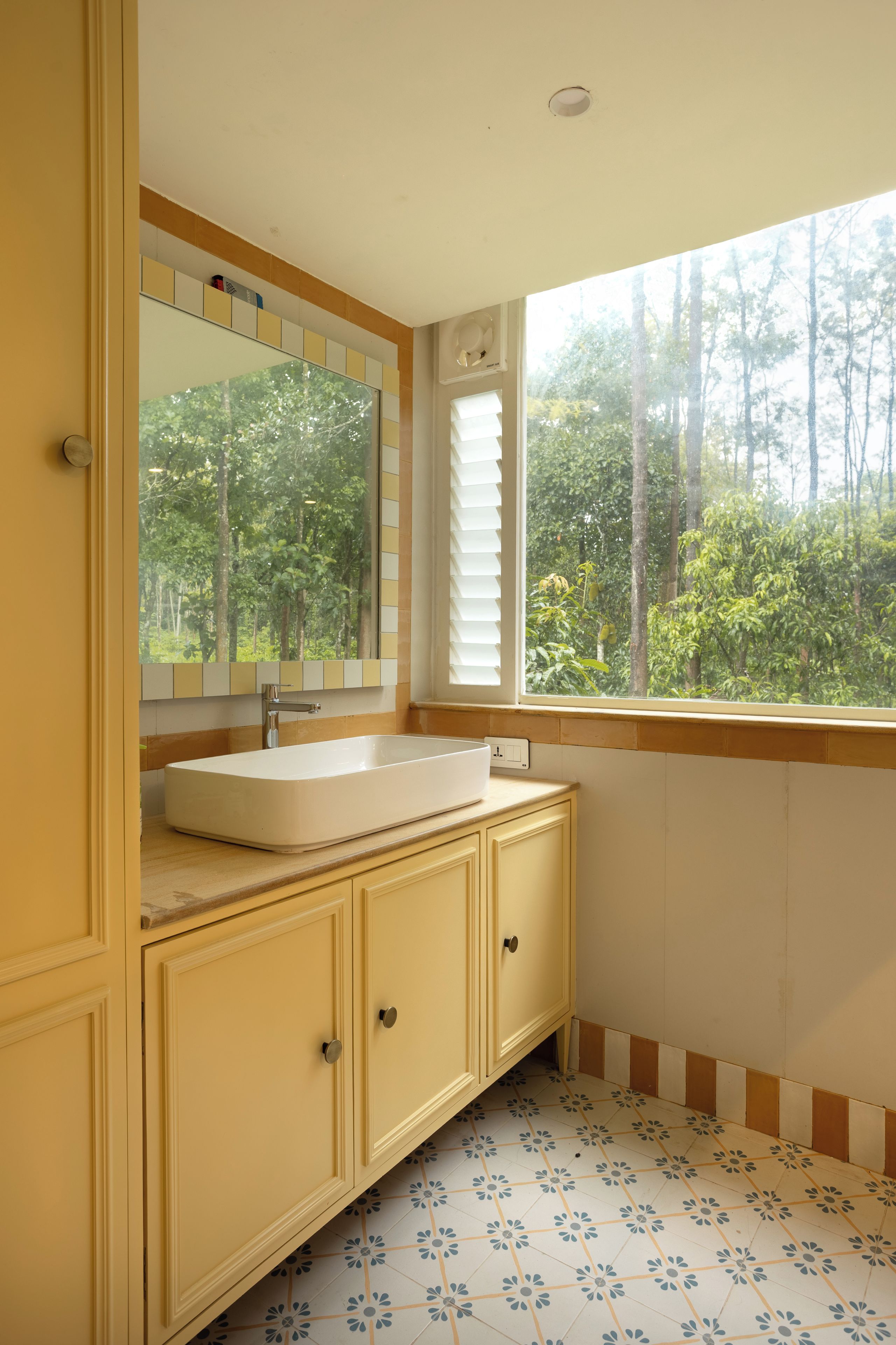 A bathroom with a white sink, a mirror above it, and a window with a view of trees.