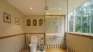 Baño con inodoro, ducha y ventana con vista al bosque.