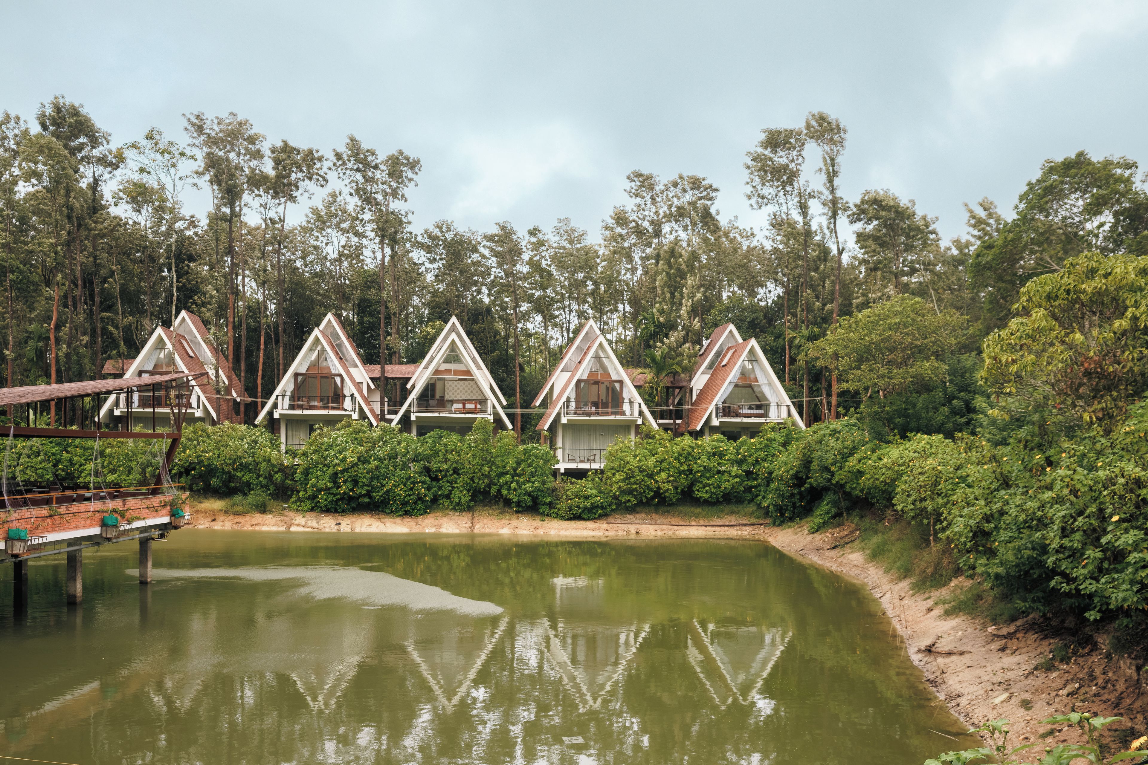A row of triangular-roofed cabins with a body of water in the foreground.