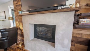 Uma sala de estar moderna com televisão de tela plana sobre a lareira, uma poltrona de couro e uma estante com livros.