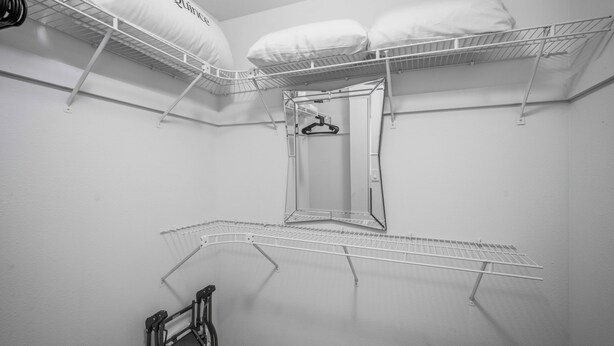 Quarto com uma cama de solteiro, um espelho e um varal de metal.