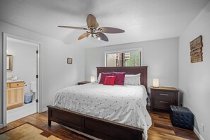 Ein Schlafzimmer mit einem Bett, Nachttischen, einem Deckenventilator, einem Fenster und einem an der Wand befestigten Kunstwerk.