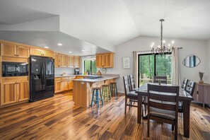 Eine moderne Küche mit Holzschränken, einem schwarzen Kühlschrank und einem Essbereich mit Tisch und Stühlen.