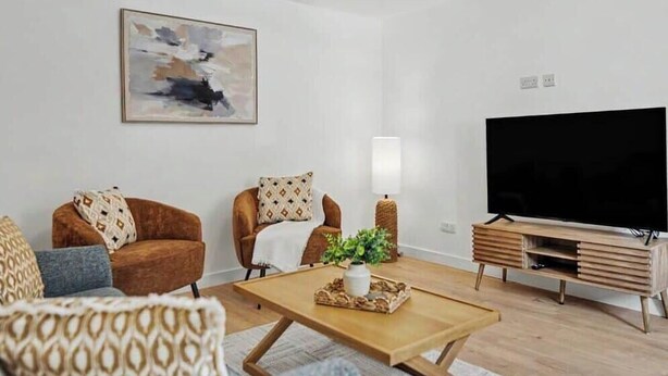 Een moderne woonkamer met een flatscreen televisie, twee fauteuils, een salontafel en een schilderij aan de muur.