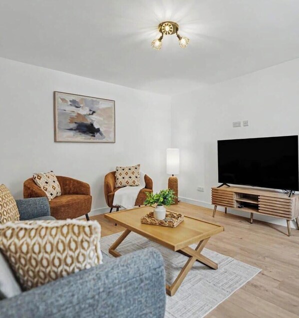 A modern living room with a flat-screen TV, two armchairs, a coffee table, and a painting on the wall. - The Den at Jamaica Street (Peterhead)