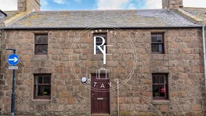 A stone building with a traditional design, featuring a central entrance door and multiple windows. - The Den at Jamaica Street (Peterhead)