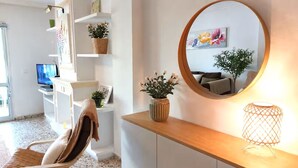 Een moderne woonkamer met een bank, een houten console tafel, een ronde spiegel en een potplant.