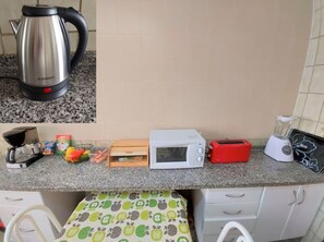 Una cocina con un hervidor de acero inoxidable, un microondas, un tostador y una licuadora sobre la encimera.