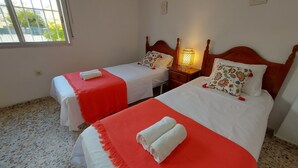 Een hotelkamer met twee eenpersoonsbedden, elk met een rood-witte spreidek en een houten hoofdbord, en een nachtkastje met een lamp.
