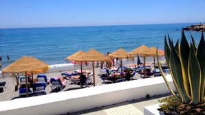 Een strand met ligbedden en rieten parasols.