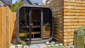 Un espacio exterior moderno y cerrado con puerta de vidrio, terraza de madera y un pequeño jardín.