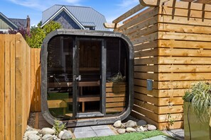 A modern, enclosed outdoor space with a glass door, wooden deck, and a small garden area. - Seabrook Newhart | Hot Tub, Sauna, Cold Plunge 9BR | Sleeps 18, Garage Parking (Pacific Beach)