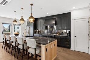 A modern kitchen with a central island, bar stools, dark cabinetry, and pendant lighting. - Seabrook Newhart | Hot Tub, Sauna, Cold Plunge 9BR | Sleeps 18, Garage Parking (Pacific Beach)