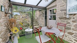 A conservatory with a glass door, stone walls, a table with a lace tablecloth, red chairs, and a vase with flowers. - View of Château de la Roche-Jagu, Nordic Bath Relaxation Area – Guest Room (Ploëzal)
