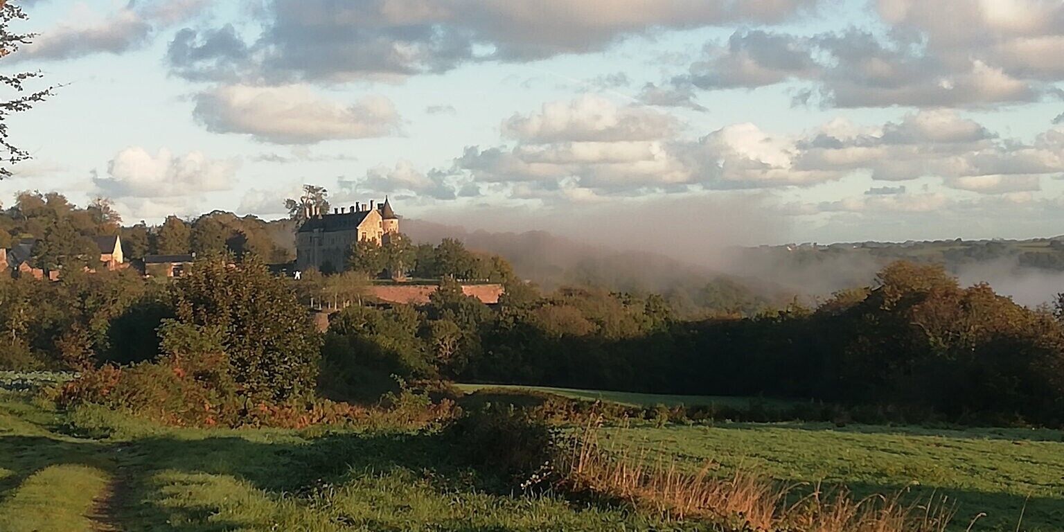 Un château entouré d’arbres et de champs, dans une atmosphère brumeuse.