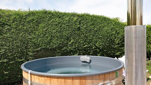 A hot tub with a wooden exterior and a metal frame, set against a backdrop of a neatly trimmed hedge. - View of Château de la Roche-Jagu, Nordic Bath Relaxation Area – Guest Room (Ploëzal)