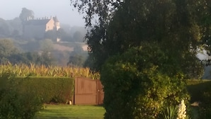 A rural landscape with a large house on a hill, a wooden shed, and a hedge in the foreground. - View of Château de la Roche-Jagu, Nordic Bath Relaxation Area – Guest Room (Ploëzal)