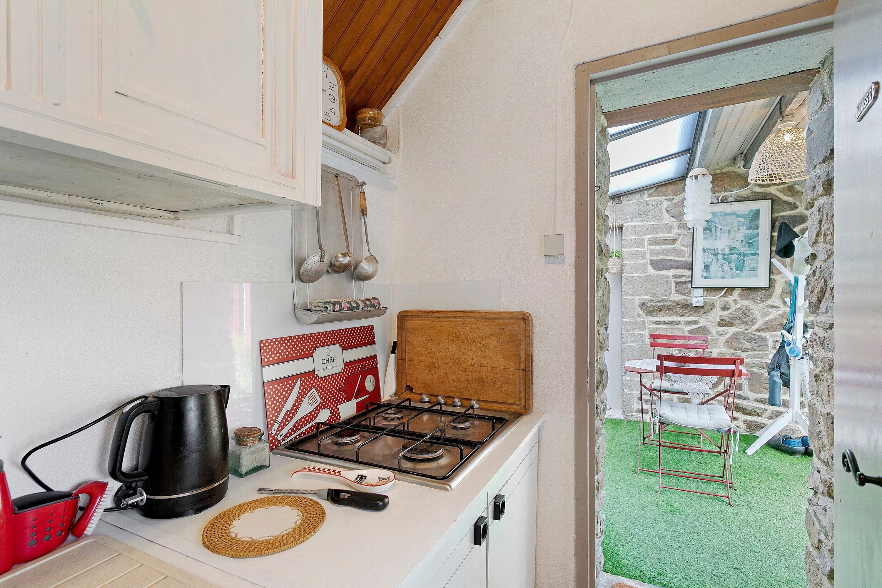 A compact kitchen with a gas stove, a coffee maker, and a red kettle.