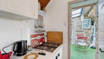 A compact kitchen with a gas stove, a coffee maker, and a red kettle.