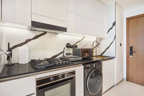 A modern kitchen with a gas stove, oven, microwave, and a built-in washing machine. - Stylish Studio with Dubai Canal & Skyline Views (Dubai)