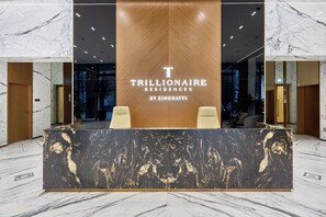 A reception desk with a marble top and a wooden panel in the center displaying the text 'TRILLIONAIRE RESIDENCES BY BINGHATTI'. - Stylish Studio with Dubai Canal & Skyline Views (Dubai)