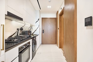 A modern kitchen with a stove, microwave, and oven. - Stylish Studio with Dubai Canal & Skyline Views (Dubai)