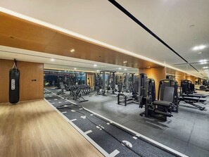 A gym with various exercise equipment, a punching bag, and a mirrored wall. - Stylish Studio with Dubai Canal & Skyline Views (Dubai)