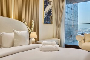 A hotel room with a large bed, a bedside table with a lamp, a view of the city through a large window, and a decorative wall panel. - Stylish Studio with Dubai Canal & Skyline Views (Dubai)