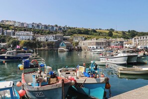 Un port amb vaixells amarrats, una construcció de pedra i edificis al fons.