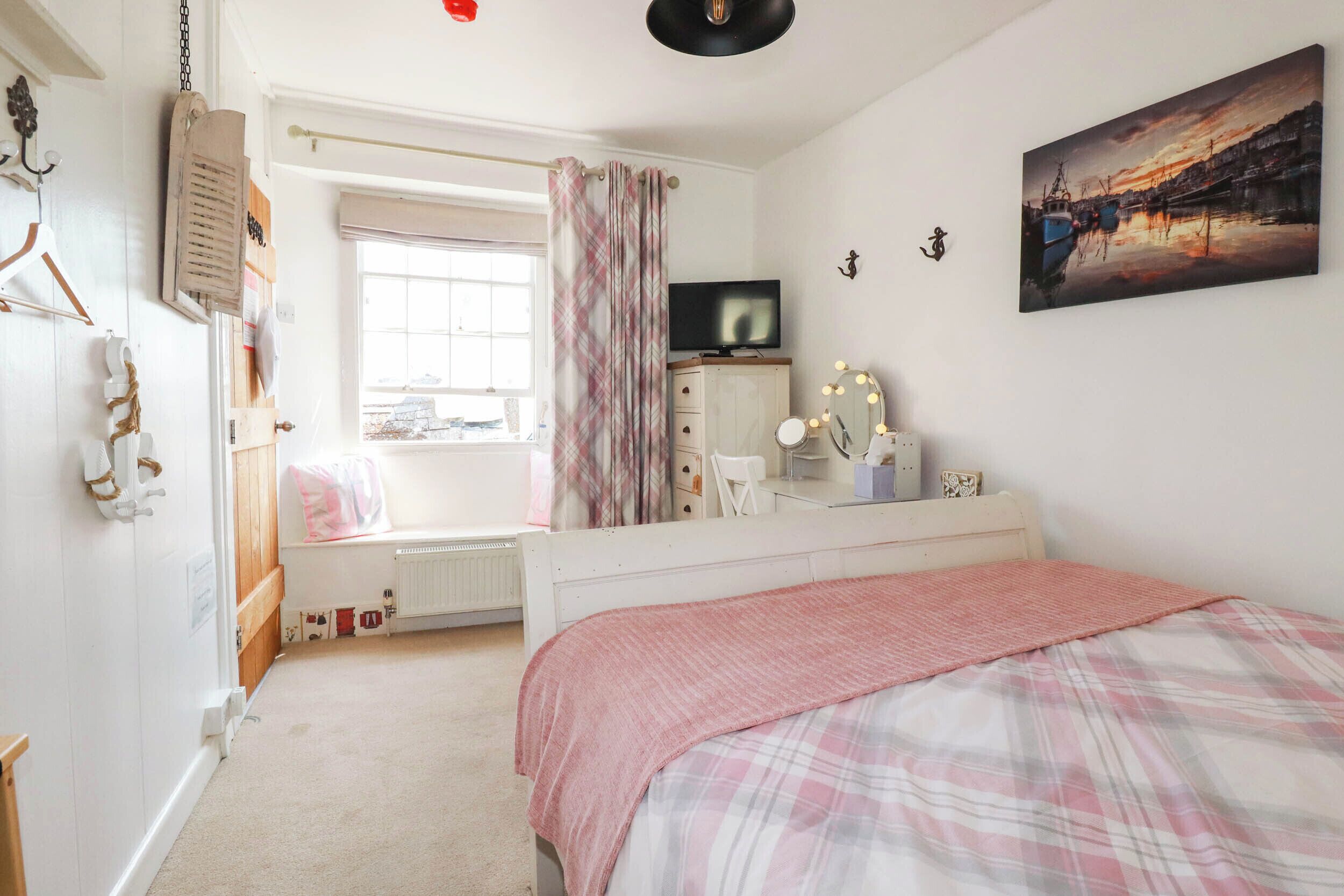 Un dormitorio con cama, cómoda, televisor y ventana con cortinas.