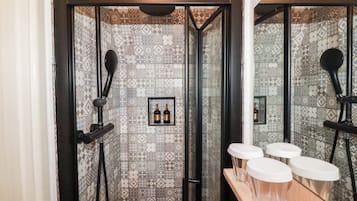 Zona de ducha con azulejos estampados, un espejo y una repisa con botellas y vasos.