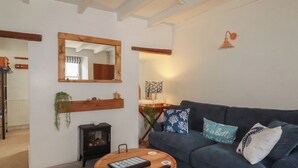 Een gezellige woonkamer met een donkerblauwe bank, een ronde houten salontafel, een zwarte houtkachel en een spiegel aan de muur.