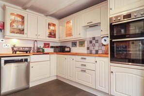 A kitchen with white cabinetry, a dishwasher, a microwave, and a double oven. - Stones Throw (St Austell)