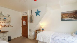 Een slaapkamer met een bed, nachtkastje, lamp, ster decoratie, spiegel, plank met spullen, en een deur met een bordje.