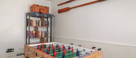Une pièce avec une table de baby-foot, une bibliothèque et deux raquettes accrochées au mur.