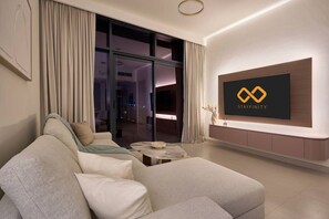 A modern living room with a sofa, a coffee table, and a flat-screen TV mounted on the wall. - Modern 1BR | Golf Views | Vista Dubai Sports City (Dubai)