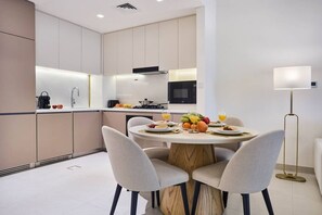 A modern kitchen with a dining area, featuring a round table with chairs, a microwave, and a sink. - Modern 1BR | Golf Views | Vista Dubai Sports City (Dubai)