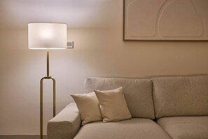 A modern floor lamp with a white shade, a beige sofa with two cushions, and a minimalist painting on the wall. - Modern 1BR | Golf Views | Vista Dubai Sports City (Dubai)