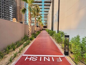 A red pathway marked 'FINISH' leading to a building with a modern design, surrounded by greenery and palm trees. - Modern 1BR | Golf Views | Vista Dubai Sports City (Dubai)