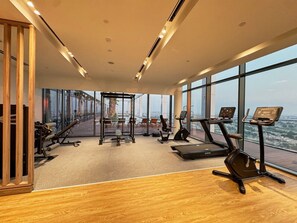 A gym with cardio machines, weight equipment, and large windows offering a city view. - Modern 1BR | Golf Views | Vista Dubai Sports City (Dubai)